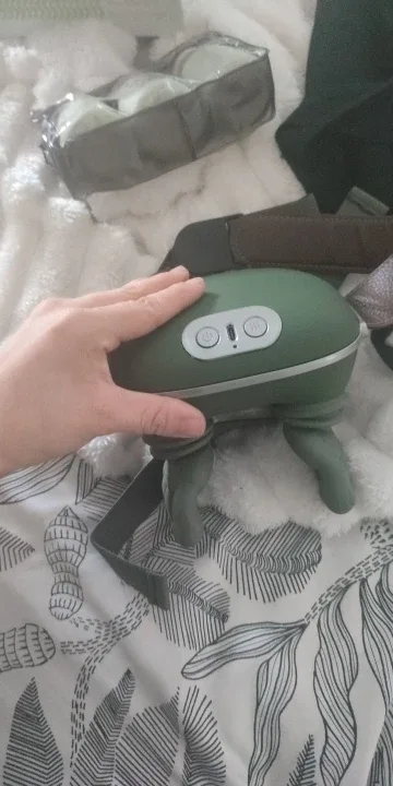 Eine Hand liegt auf dem Massagegerät, das auf gemusterter Bettwäsche steht, das Bedienfeld unter den Fingern
